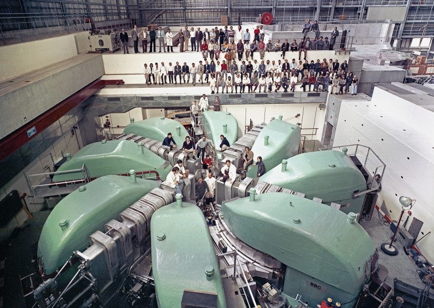 Wie auf dem Rücken von Dinosauriern: Im Jahr 1973, kurz bevor die Protonenanlage in Betrieb ging, liess sich die Belegschaft am grossen Ringzyklotron fotografieren. (Foto: Paul Scherrer Institut)