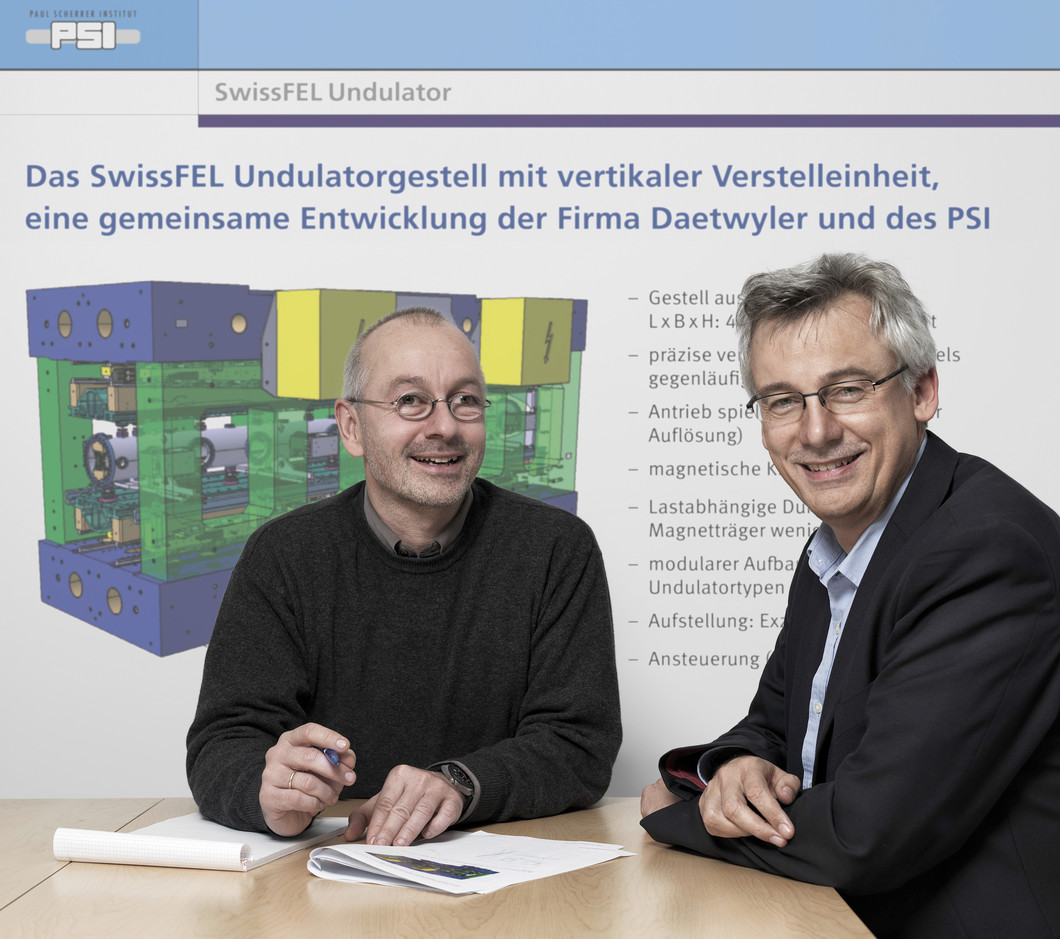 Thomas Schmidt, responsable du développement des onduleurs et Hans Braun, Chef de Projet du projet SwissFEL devant un dessin technique représentant un onduleur. (Scanderbeg Sauer Photography)