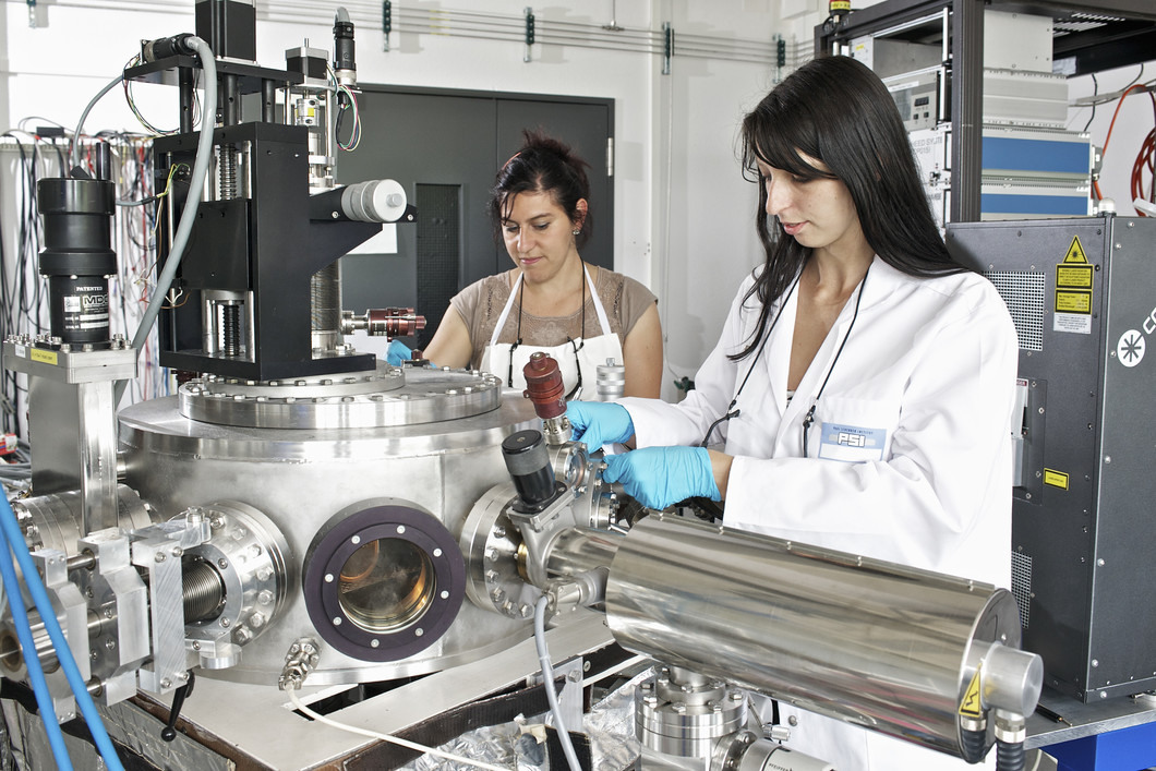 Die Forscherinnen Claudia Cancellieri und Mathilde Reinle-Schmitt an einer Anlage, an der mit Hilfe eines Lasers dünne Schichten von unterschiedlichen Materialien hergestellt werden können. (Foto: Paul Scherrer Institut/M. Fischer)