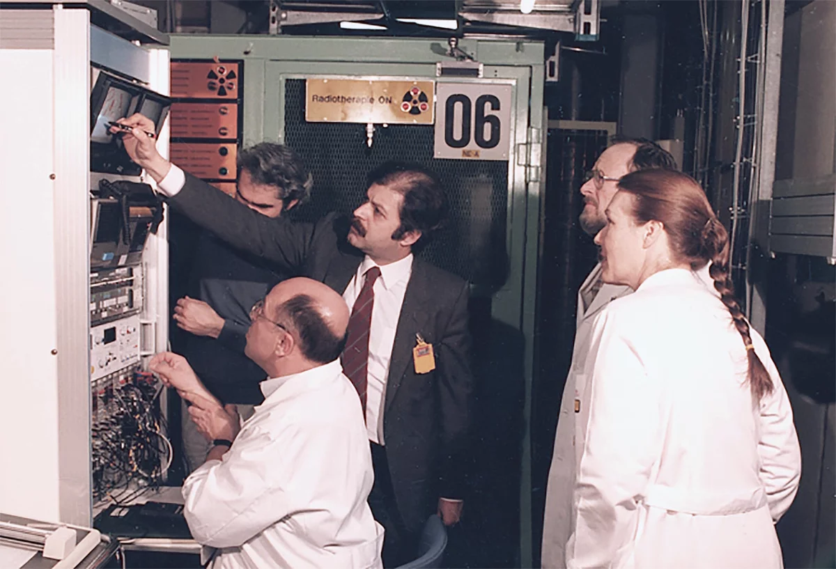 The OPTIS team in the control room during treatment of the first patients in March 1984. Two initiators of the of the project are present: Charles Perret (sitting) and Leonidas Zografos (third from right, standing). 