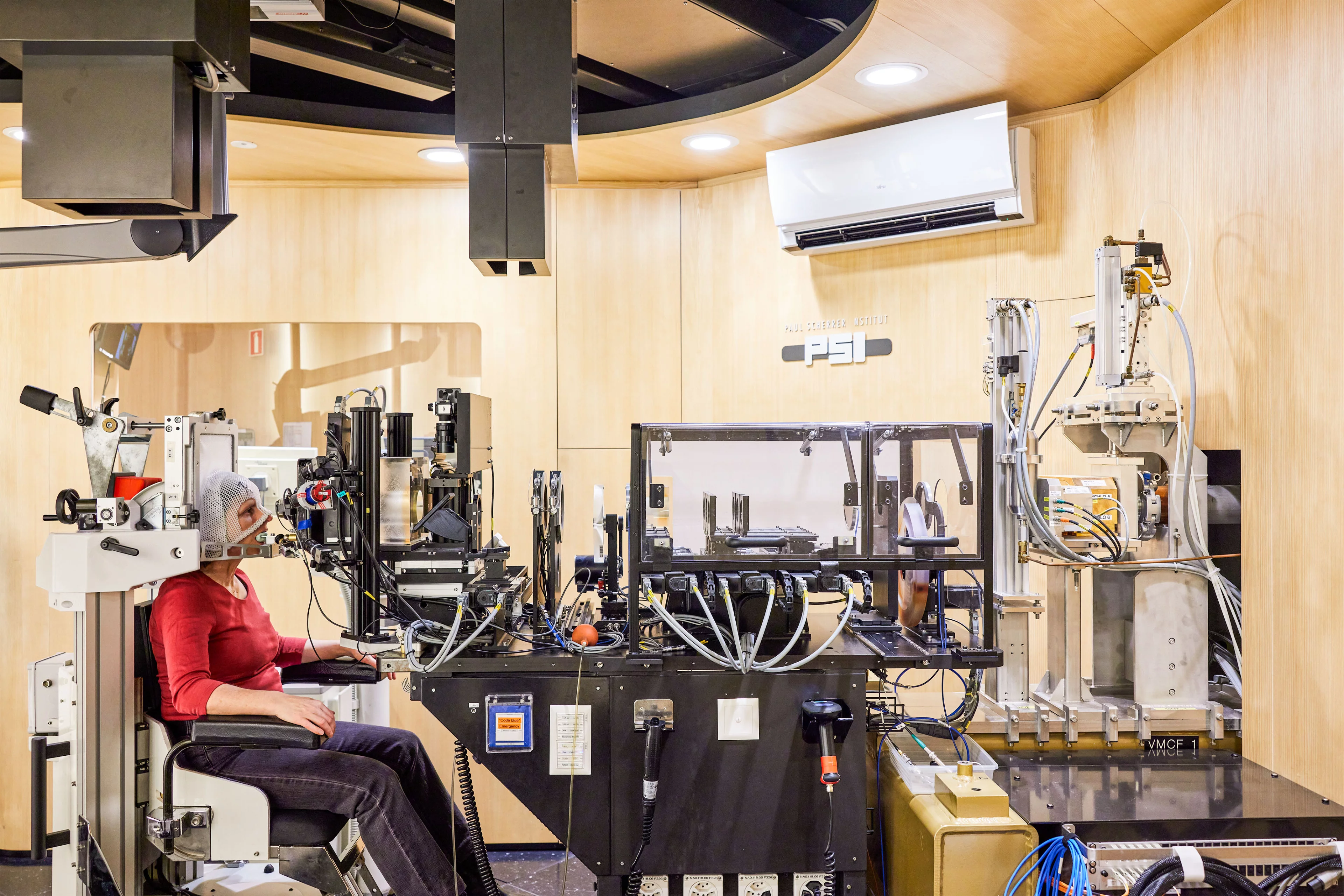 L’installation d’irradiation OPTIS 2: le faisceau de protons (arrivant depuis la droite sur la photo) est adapté à la taille et à l’énergie requises pour traiter cette tumeur spécifique. La patiente regarde le faisceau de protons de face et doit orienter son œil de telle sorte que la tumeur se trouve exactement dans le trajet des rayons. Elle-même est fixée dans le fauteuil de traitement avec un masque et un appui buccal afin d’éviter qu’elle ne bouge et ne compromette le succès du traitement. 