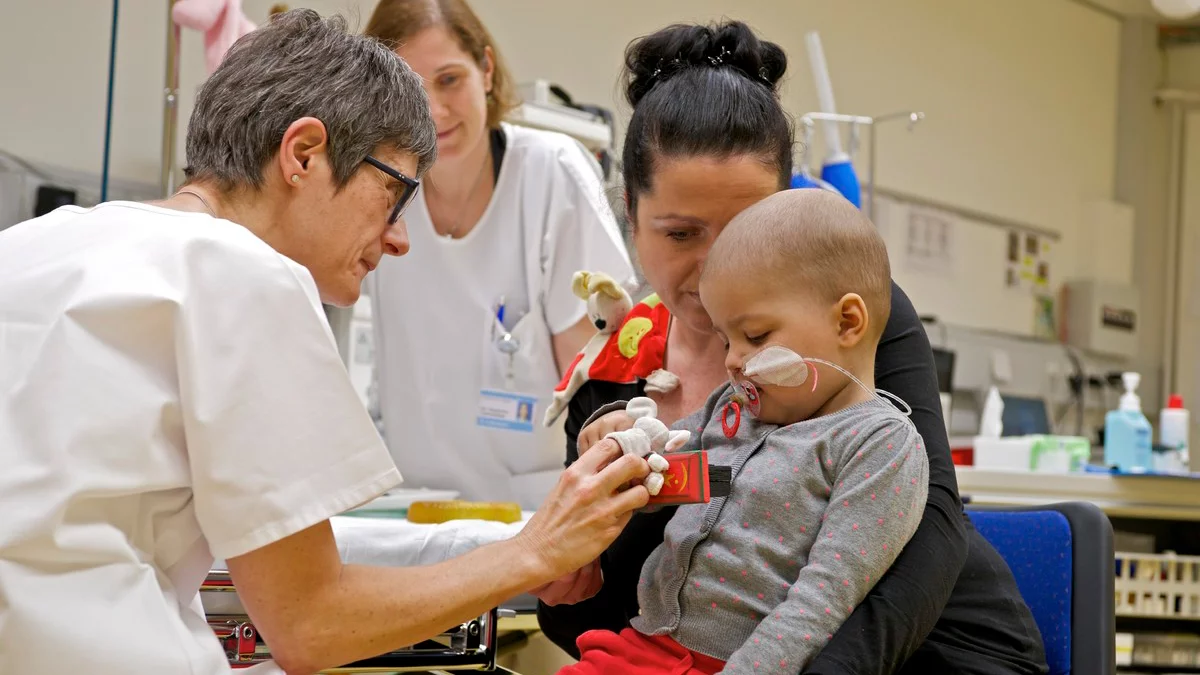 Schon kleine Kinder werden am Zentrum für Protonentherapie ZPT des Paul Scherrer Instituts PSI mit Protonen gegen ihren Krebs bestrahlt. Einige von ihnen bekommen eine Narkose. Dieses Kind sitzt auf dem Schoss seiner Mutter und wird durch die Narkoseärztin (links im Bild) mit einem Fingerpuppenspiel beruhigt, bevor die Behandlung losgeht. (Foto: Paul Scherrer Institut/Markus Fischer)