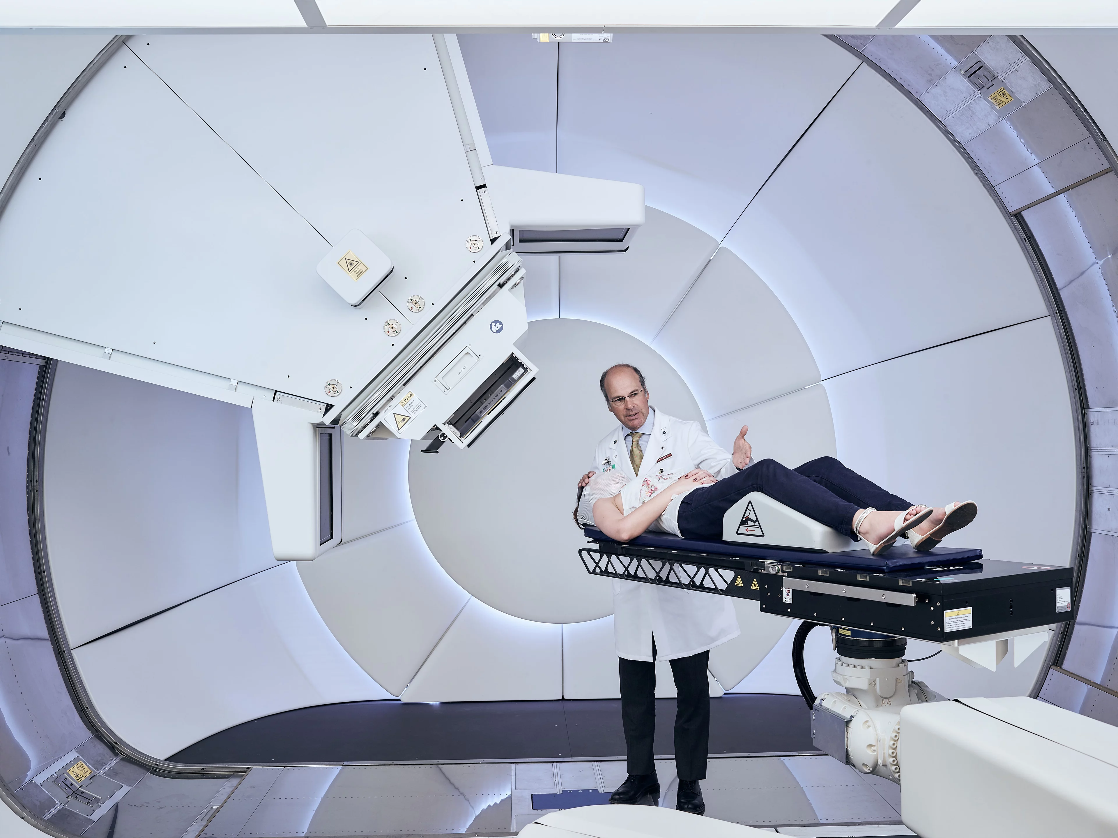 Gantry 3 – der neue Behandlungsplatz für Protonentherapie am Paul Scherrer Institut PSI. Eine Mitarbeiterin des PSI demonstriert die Patientenpositionierung. Stehend: Prof. Damien Weber, Leiter des Zentrums für Protonentherapie am PSI. (Foto: Scanderbeg Sauer Photography)