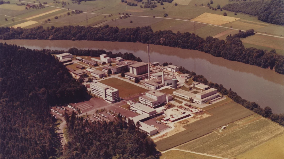 Damals befand sich auf der Ostseite des heutigen PSI-Campus das Eidgenössische Institut für Reaktorforschung. Der charakteristische Donut der Synchrotron Lichtquelle Schweiz SLS und die Aarebrücke zwischen Würenlingen und Villigen existierten noch nicht. Das Hotlabor (L-förmiges Gebäude ganz rechts im Bild) gehört heute zu den ältesten Gebäuden auf dem Campus.
