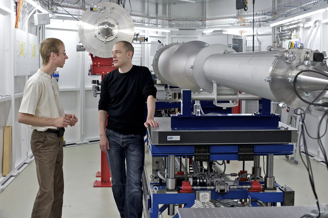 PSI scientists Oliver Bunk and Andreas Menzel beside the detector chamber of the measuring station cSAXS at the SLS. The detector registering the deflected x-rays is at the wide end of the long tube, the investigated sample is placed in front of the narrow end visible in the foreground.  Copyright: Paul Scherrer Institute/M. Fischer