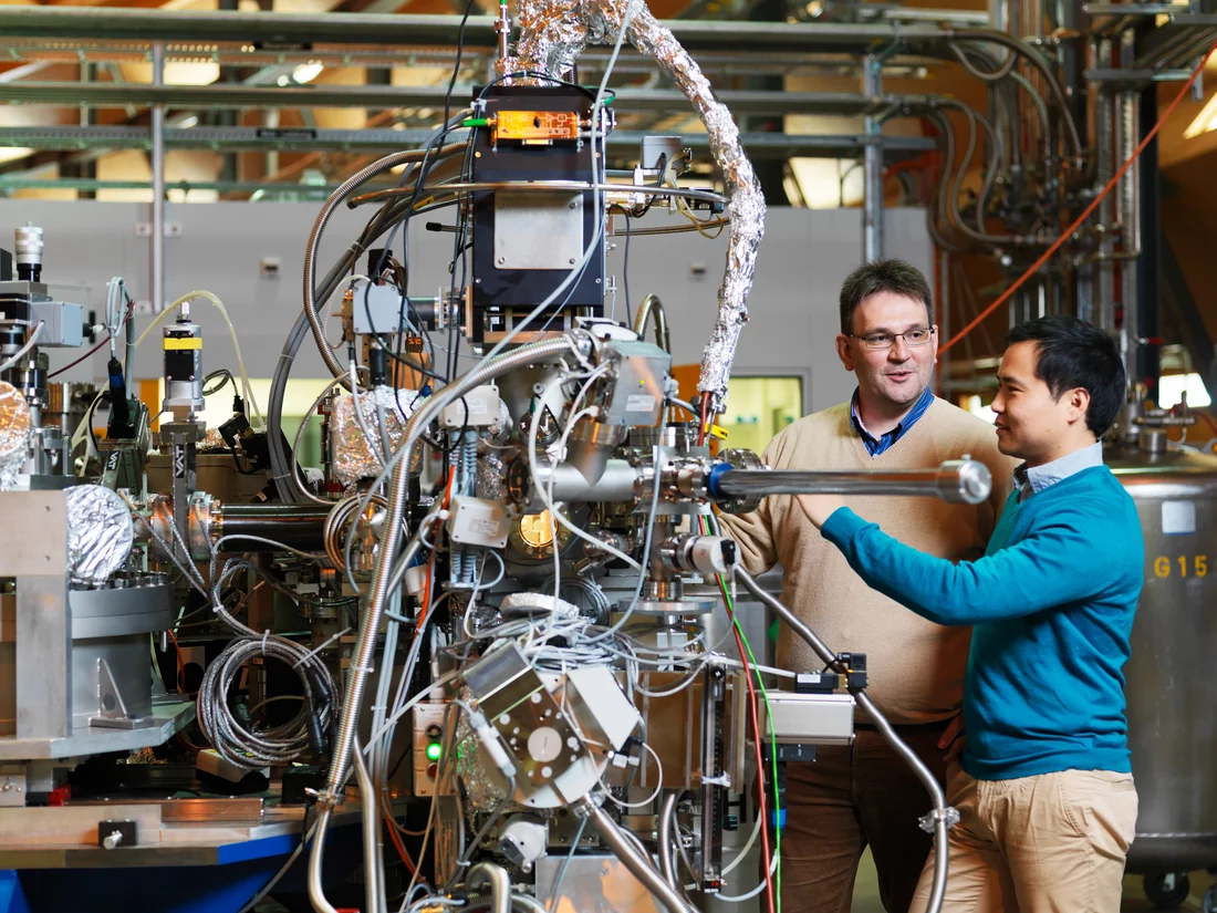 Thorsten Schmitt (à gauche) et Kejin Zhou (à droite), chercheurs au PSI Chargement d'un échantillon de matériau dans l'installation de mesure au poste RIXS de la ligne de lumière ADRESS. Les rayons X permettent ici l'analyse de matériaux avec une précision très élevée. (Photo : Scanderbeg Sauer Photography)