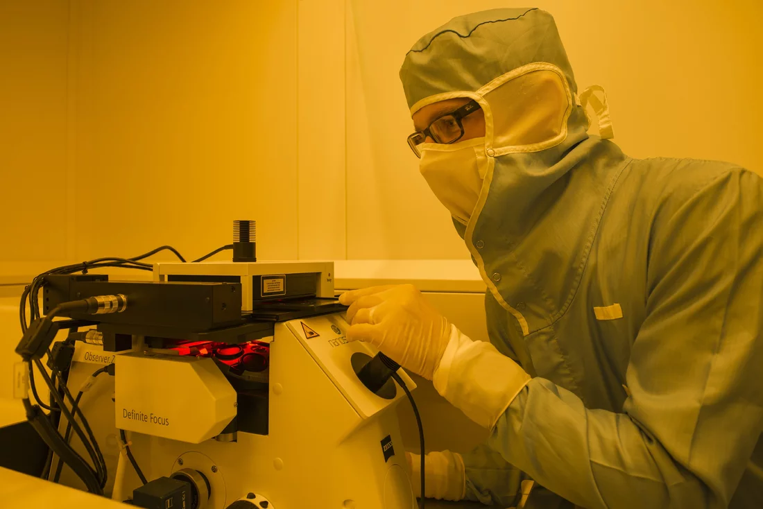 Robert Kirchner, chercheur au PSI, avec l’appareil laser au moyen duquel les maquettes du Cervin de sept centièmes de millimètre ont été fabriquées. Le chercheur porte une combinaison protectrice qui protège l’appareil de la poussière, des poils et des cheveux. La salle est éclairée en jaune, car les maquettes sont fabriquées à partir d’un matériau photosensible sur lequel la lumière jaune n’a pas d’impact. (Photo: Institut Paul Scherrer/Mahir Dzambegovic)
