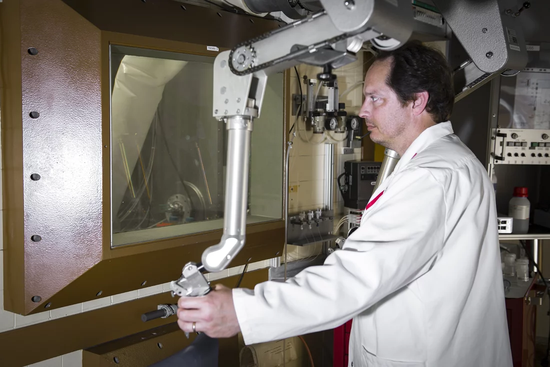 The radiochemist Nick van der Meulen working at a hot cell with the help of manipulators. Protection from samples of the radioactive nuclide scandium-44 is provided by a 36 cm-thick pane of lead glass. (Photo: Paul Scherrer Institute/Mahir Dzambegovic)