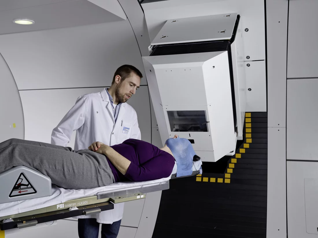 A medical-technical assistant prepares the patient for proton irradiation at Gantry 2 of the Paul Scherrer Institute. The patient’s head is immobilised with a special mask – this ensures that the proton beam precisely hits the tumour. (Photo: Scanderbeg Sauer Photography)