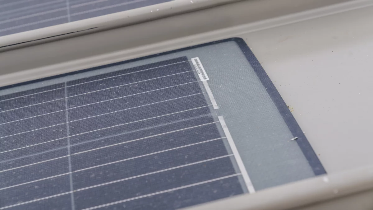 Un module solaire pénètre dans l'image par la gauche; on voit son extrémité à droite. Il est placé sur la partie plate d'un profil en aluminium peint en gris.