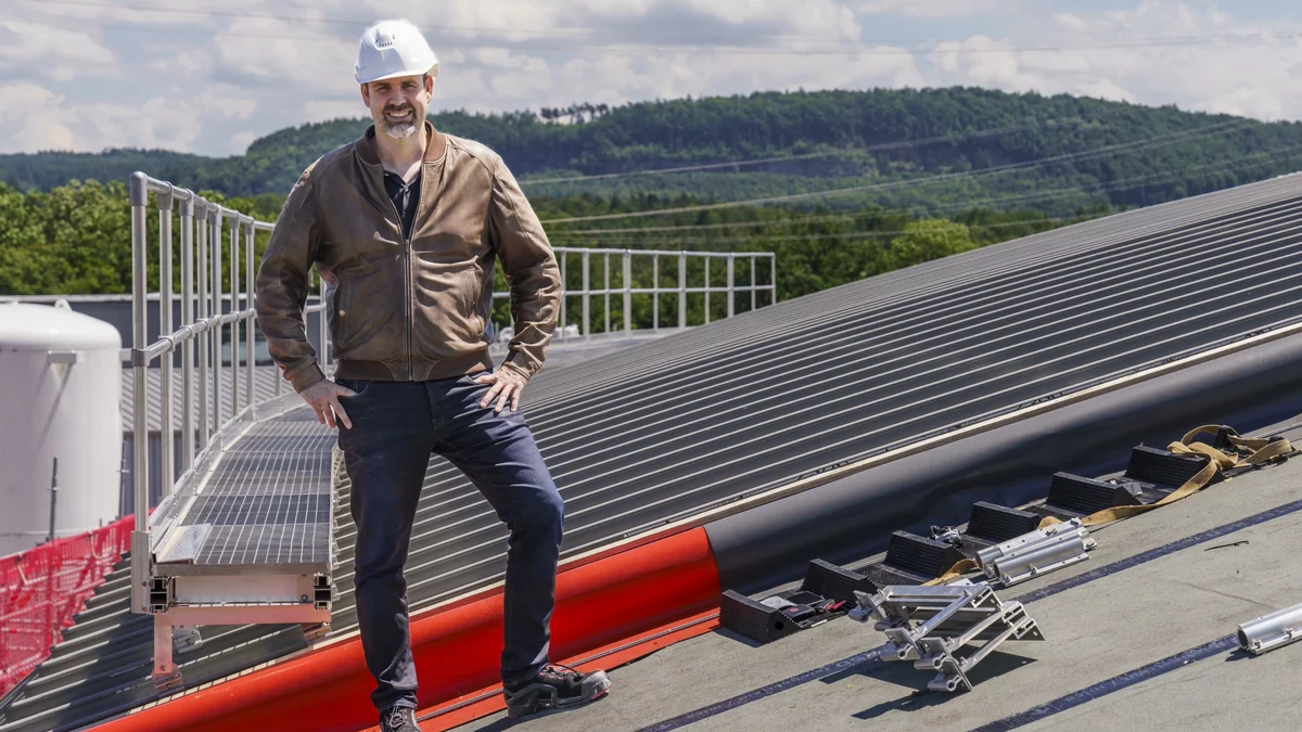 Un homme vêtu d'une veste en cuir marron et d'un casque blanc sur la tête se trouve sur le toit de la SLS. Derrière lui, on voit les premiers profils en aluminium déjà installés avec des modules solaires intégrés.