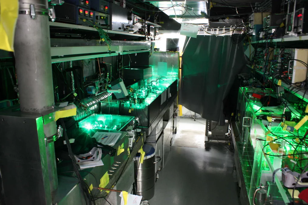 Some impressions of our laser hut. On the right there is the continuous wave (cw) part of our laser system. This is mainly composed by a frequency stabilized and tunable TiSa laser (in green). On the left you see the pulsed oscillator-amplifier system TiSa laser (in green-blue). The Raman cell (horizontal metallic tube) is partially visible left of the pulsed TiSa laser. The vertical metallic tube (left in front) transports the 6 micrometer radiation from the laser hut to the target region avoiding water a…