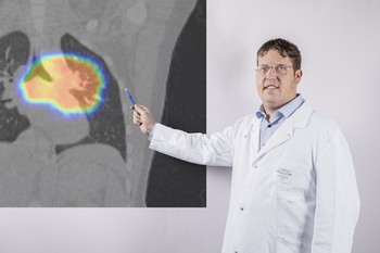 Dominic Leiser, the attending radiation oncologist of the first patient being cared for at PSI as part of the study. In the background is the computed tomography image of a patient with lung carcinoma. The area scanned by the proton beam is highlighted in colour.
