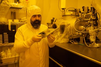 Dimitrios Kazazis dans la salle blanche à la ligne de faisceau. Il tient dans ses mains ce qu’on appelle un wafer, qui a été traité là avec le nouveau procédé. 