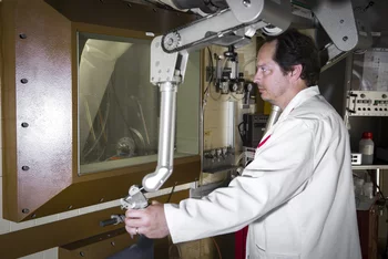 The radiochemist Nick van der Meulen working at a hot cell with the help of manipulators. Protection from samples of the radioactive nuclide scandium-44 is provided by a 36 cm-thick pane of lead glass. (Photo: Paul Scherrer Institute/Mahir Dzambegovic)