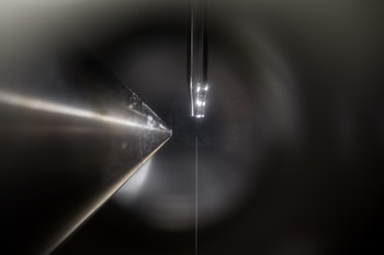 La chambre d’expérience abrite un jet d’eau vertical très fin qui jaillit d’un petit tube au milieu de l’image et coule vers le bas. Durant l’expérience, elle est remplie d’un mélange gazeux contenant de l’ozone qui réagit à la surface avec le bromure qui se trouve dans l’eau et provoque l’apparition du brome. En étape intermédiaire, une liaison de bromure et d’ozone apparaît brièvement. Cette liaison a pu être détectée pour la première fois grâce à de la lumière de type rayons X issue de la SLS. Le procéd…