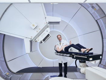 Gantry 3 – the new treatment unit for proton therapy at PSI. A staff member of PSI demonstrates the patient positioning. Standing: Prof. Damien Weber, head of the Centre for Proton Therapy at the Paul Scherrer Institute. (Photo: Scanderbeg Sauer Photography)