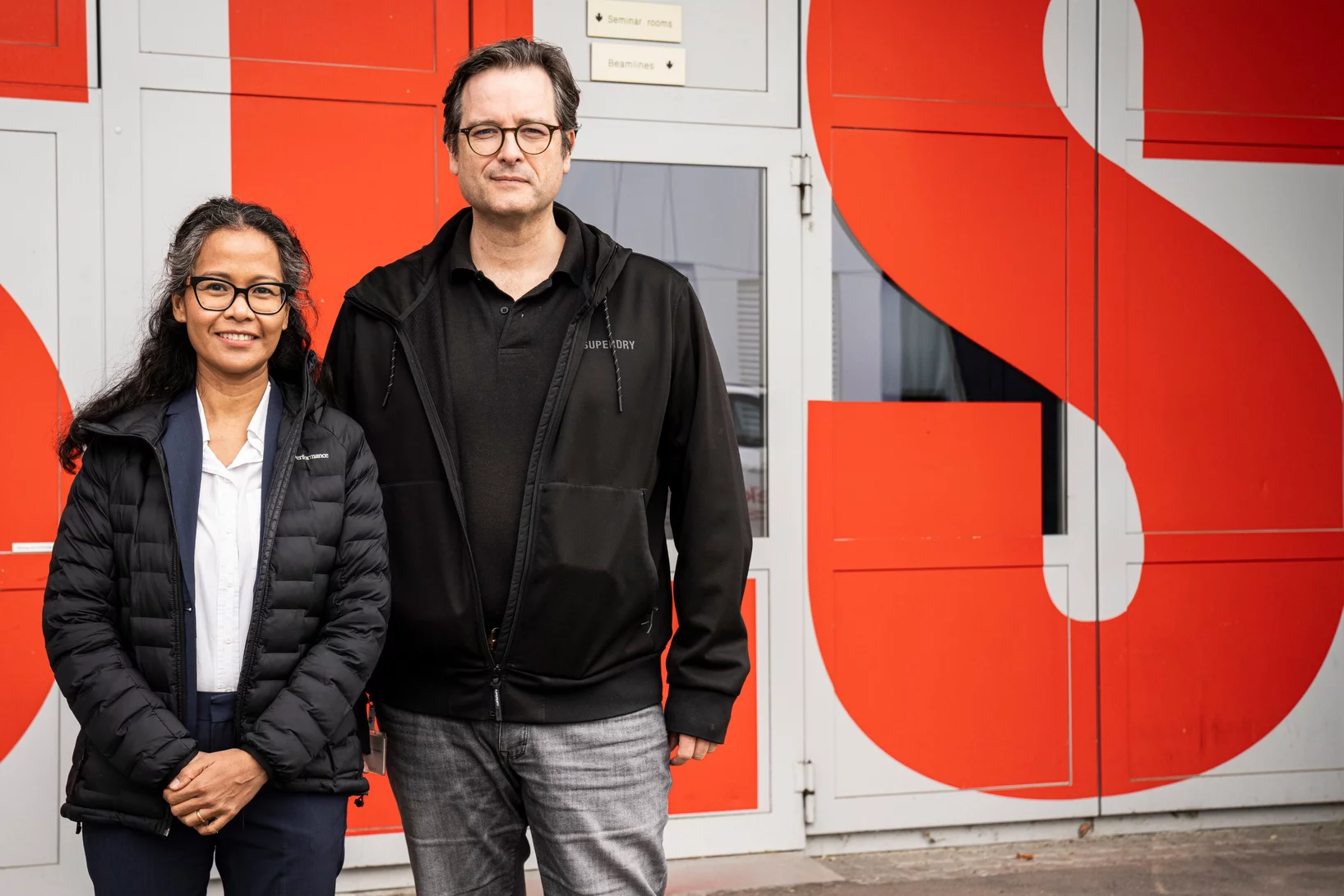 Margie Olbinado und David Mannes vor dem Eingang zur Synchrotron Lichtquelle Schweiz SLS, in der die Untersuchungen mit Synchrotronlicht durchgeführt wurden. In unmittelbarer Nachbarschaft dazu liegt auf dem Gelände des PSI die Schweizer Spallations-Neutronenquelle SINQ, die Neutronen für weitere Analysen liefert.