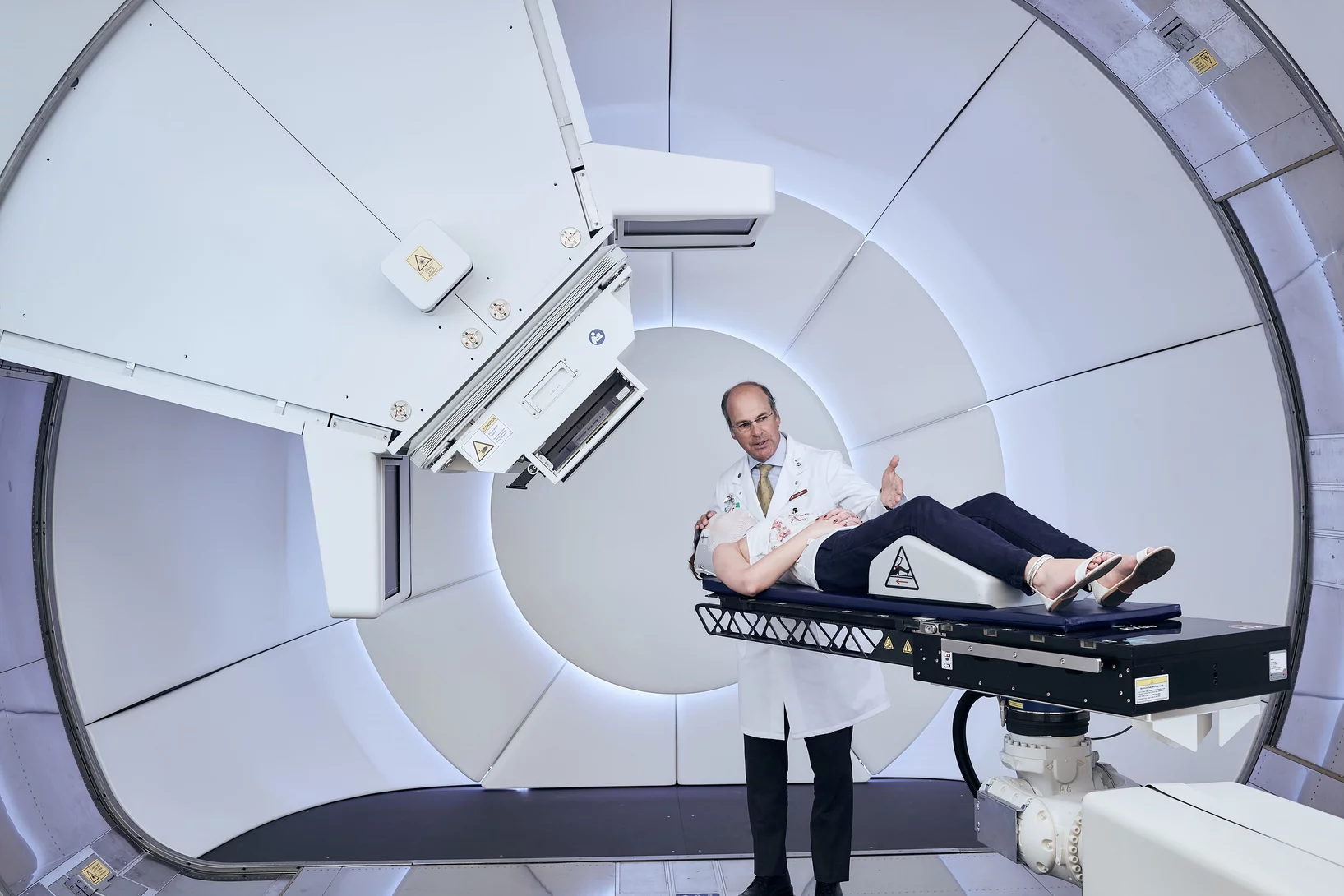 La nouvelle station de traitement par protonthérapie Gantry 3 à l'Institut Paul Scherrer PSI. Une collaboratrice du PSI est en train de montrer comment se déroule le positionnement du patient. Debout: le Pr Damien Weber, directeur du Centre de protonthérapie au PSI. (Photo: Scanderbeg Sauer Photography)